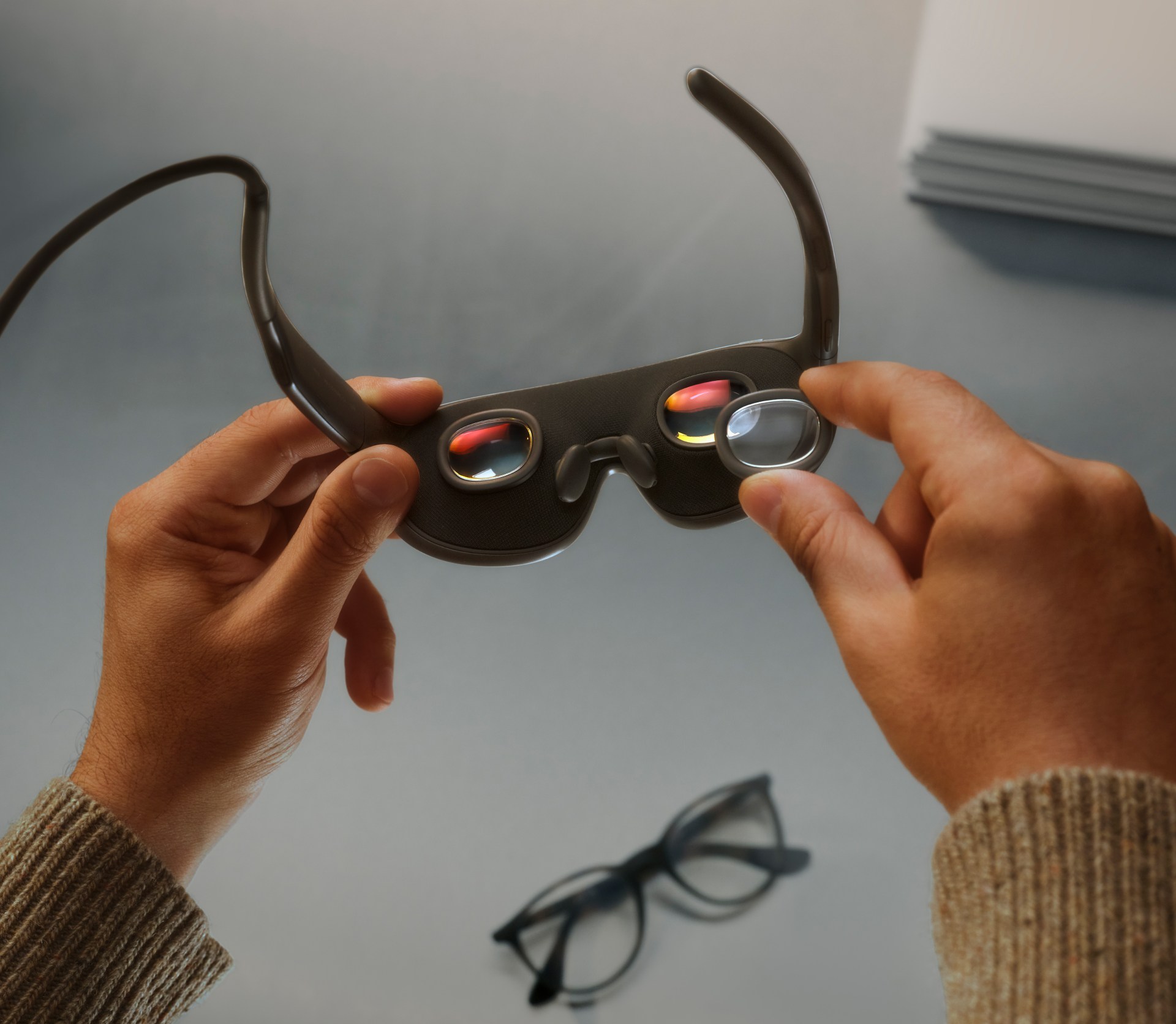 Hands holding Meta’s new VR glasses, fitting a prescription lens insert